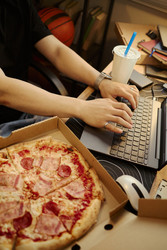 Азиат печатает на клавиатуре ноутбука, поедая пиццу за рабочим столом - DragonImagesAsia