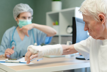 пожилой мужчина обращается к врачу во время медицинской консультации. пожилой пациент с забинтованной рукой обращается за профессиональной помощью в клинику. хрупкость костей и остеопороз - проблемы пожилых людей - ElenaSk