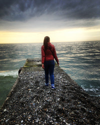 Девушка идет по пирсу в бушующее море под густыми серыми тучами - OlgaK