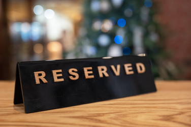 Черная табличка reserved с деревянной надписью на теплом деревянном столе. Мягкое боке-освещение на заднем плане наводит на мысль о праздничной обстановке - olinchuk
