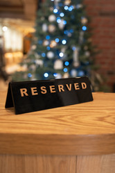 Черная табличка reserved с деревянной надписью на теплом деревянном столе. Мягкое боке-освещение на заднем плане наводит на мысль о праздничной обстановке - olinchuk