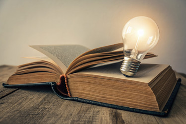 Открытая книга рядом со светящейся лампочкой для генерирования творческих идей с помощью искусственного интеллекта - RomanZ