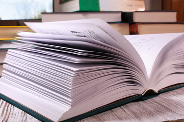 Раскрытая книга на столе на фоне стопки книг и окна - nkaup