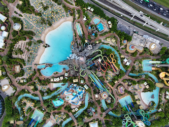 7 июля 2026 года полет беспилотника над аквапарком Volcano Bay с вулканом, бассейнами, горками и близлежащим движением на шоссе в Орландо, Флорида, США. g - EOS_Canon