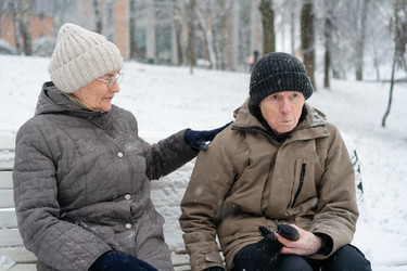 пожилая пара на скамейке в безмятежном зимнем парке, женская рука на плече мужчины. спокойная нежная пара, разделяющая мирный нежный момент в холодный день. тихие компаньоны, обретающие безмятежность рядом с заснеженными деревьями - ElenaSk
