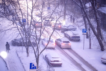 заснеженная уличная сцена с множеством транспортных средств, застрявших в пробке во время сильного снегопада, деревьями и знаками парковки, видимыми на заднем плане - Darya Petrenko