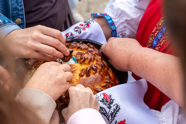 крупный план рук людей, берущих кусочки традиционного украшенного круглого хлебного каравая (коровай/каравай-вай) во время славянского народного праздника или свадебной церемонии - DmitryKurullin
