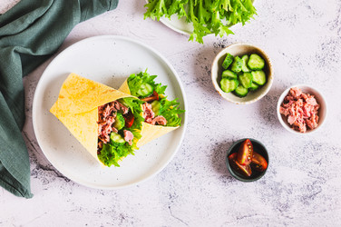 Вкусные тако с консервированным тунцом, огурцом, помидором и листьями салата на тарелке на столе, вид сверху - Elena Rui