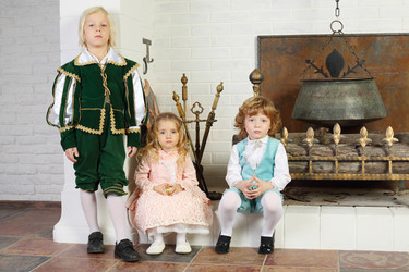 Two boys and girl in medieval costumes pose near fireplace - paha_l