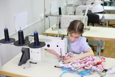 Student girl sews small dress at white sewing machine in - paha_l