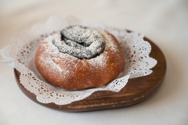 Свежеиспеченная булочка с маком, посыпанная сахарной пудрой, подается на деревянной тарелке с кружевной салфеткой в уютной минималистской обстановке - olinchuk
