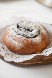 свежеиспеченная булочка с маком, посыпанная сахарной пудрой, подается на деревянной тарелке с кружевной салфеткой в уютной минималистской обстановке - olinchuk