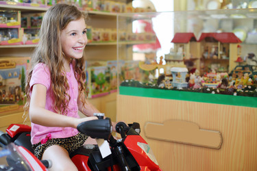 Little cute girl in sits on red toy motorcycle in store with toys - paha_l