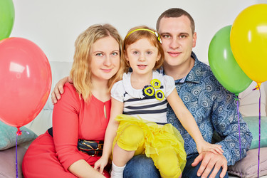Family of three sits on sofa in light room decorated with - paha_l