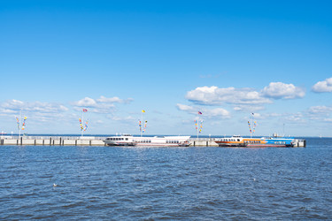 Широкий горизонтальный вид пассажирских паромов на подводных крыльях, пришвартованных к причалу в Петергофе, Санкт-Петербург. Живописный морской транспортный фон над спокойной водой Невской губы под голубым летним небом с копировальным пространством - IKvyatkovskaya