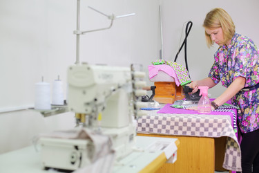 Симпатичная женщина-портной гладит новую футболку в полоску возле швейной машинки - paha_l