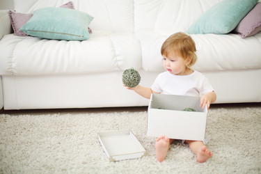 Little in white sits on carpet near white sofa and holds box - paha_l