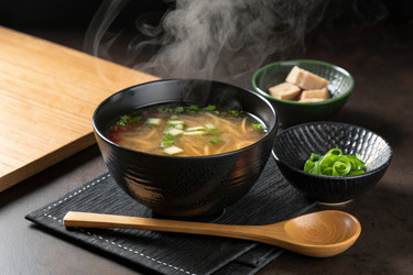 Вкусный горячий суп подается в черной миске с гарнирами на деревянном столе - RomanZ