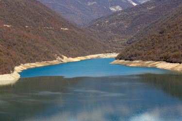 лесистые склоны и берег жинвальского водохранилища, искусственного озера, расположенного на реке арагви в горах кавказа в грузии. осенний пейзаж, путешествия и изучение природы - gumbao