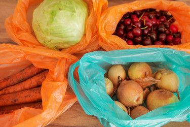 Продуктовые овощи, упакованные в разноцветные пластиковые пакеты для покупок, на деревянном столе. Концепция покупки свежих продуктов и снабжения домашних хозяйств продуктами питания - Gannachka