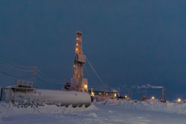 An illuminated oil and gas drilling rig operates in the harsh conditions of the Arctic winter. A snow‑covered industrial landscape during the polar night. Energy resource extraction - Vkadimir