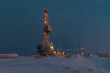 An illuminated oil and gas drilling rig operates in the harsh conditions of the Arctic winter. A snow‑covered industrial landscape during the polar night. Energy resource extraction - Vkadimir