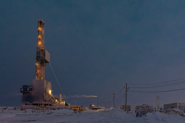 An illuminated oil and gas drilling rig operates in the harsh conditions of the Arctic winter. A snow‑covered industrial landscape during the polar night. Energy resource extraction - Vkadimir