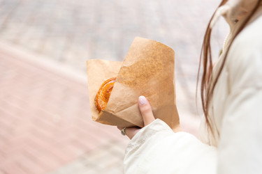 Женщина, идущая по городской улице, держит в руках вкусную выпечку в коричневом бумажном пакете - AliakseiSmalenski
