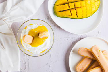 вкусный десерт с манговым пюре, йогуртом и печеньем савоярди в миске на столе вид сверху - Elena Rui