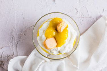крупный план вкусного десерта с манговым пюре, йогуртом и печеньем савоярди в миске на столе вид сверху - Elena Rui