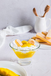 вкусный десерт с манговым пюре, йогуртом и печеньем савоярди в миске на столе вертикальный вид - Elena Rui