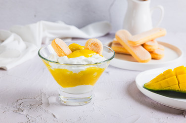 вкусный десерт с манговым пюре, йогуртом и печеньем савоярди в миске на столе - Elena Rui