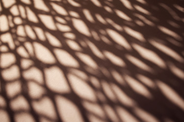 замысловатые теневые узоры, отбрасываемые на текстурированную поверхность, демонстрируют похожий на паутину дизайн, созданный за счет фильтрации света через решетчатую структуру - Darya Petrenko