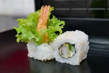 крупным планом японские суши-роллы с креветками темпура, огурцом и кунжутом на черной тарелке. традиционная азиатская кулинарная фотография - Gannachka