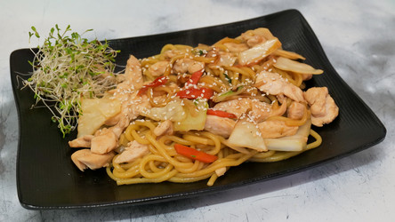 азиатское блюдо из лапши с жареной курицей или рыбой и овощами подается на черной прямоугольной тарелке с микрозеленью. горячее блюдо с лапшой и концепция ресторанной кухни - Gannachka