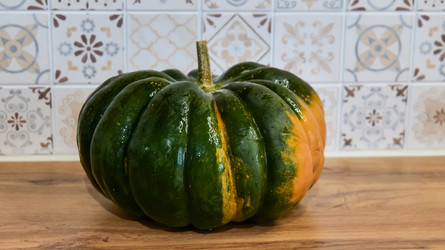 Нейтрально-зеленая тыква, стоящая на деревянной кухонной стойке с облицованной плиткой задней панелью, вид спереди, фотография еды, декор кухни, естественное освещение, чистый фон - Gannachka