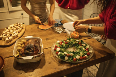 группа людей готовит праздничное блюдо с жареным мясом, овощным ассорти и закусками на деревянном столе в уютной кухонной обстановке во время праздничного сбора - Darya Petrenko