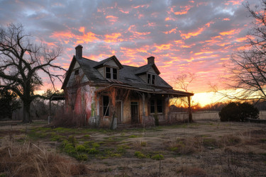 Abandoned house is slowly decaying in a field as the sun sets in the background - yliv