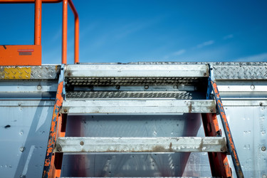 Old metal industrial staircase leading upwards on the side of a building against a blue sky - yliv