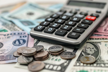 Accountant calculating expenses using calculator on desk with dollar bills and coins - yliv