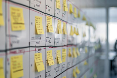 Доска рабочего процесса по методологии Agile scrum, покрытая желтыми стикерами для заметок, в современном бизнес-офисе - yliv