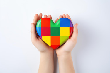 Child's hands gently holding a vibrant, puzzle piece heart, symbolizing autism awareness, acceptance, and neurodiversity support - yliv