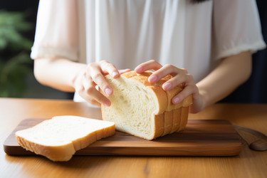 Woman taking a slice of bread from a loaf on a wooden board - yliv