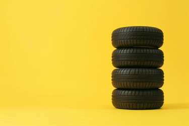 Four car tires stacked vertically on a vibrant yellow background, forming a striking composition - yliv