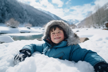 Happy child lying in snow by frozen river in winter wonderland - yliv