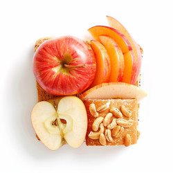Whole and sliced apples and apricots creating a face on multigrain toast - yliv