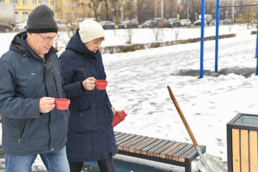 пара вместе наслаждается теплыми напитками в зимнем парке, пока землю покрывает снег - VetalanaS