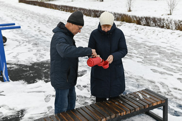 пара вместе наслаждается теплыми напитками в зимнем парке, пока землю покрывает снег - VetalanaS