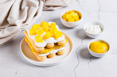 Delicious tiramisu with cookies, mango purée, and cream cheese, served on a plate on a table - Elena Rui