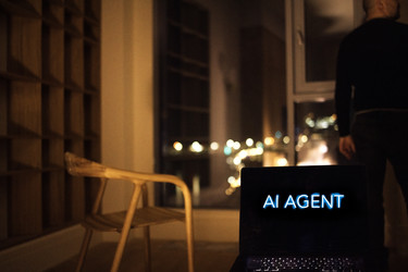 ноутбук с дисплеем "агент искусственного интеллекта " в тускло освещенной современной комнате с деревянным стулом и человеком, стоящим у большого окна с видом на городские огни - Darya Petrenko